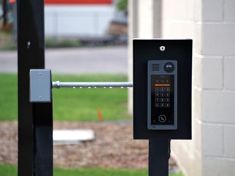 A pedestal-mounted intercom and keypad at a gated entrance.