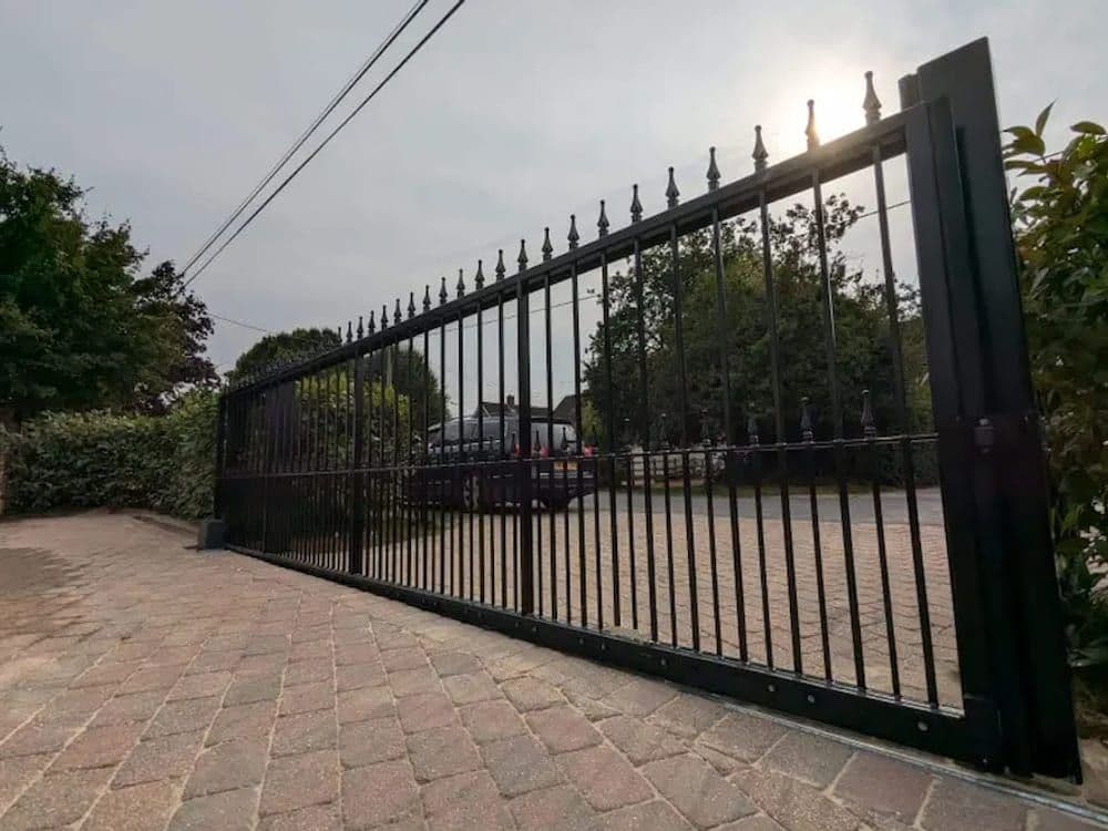 A powered cantilever sliding gate standing closed across a block-paved driveway.